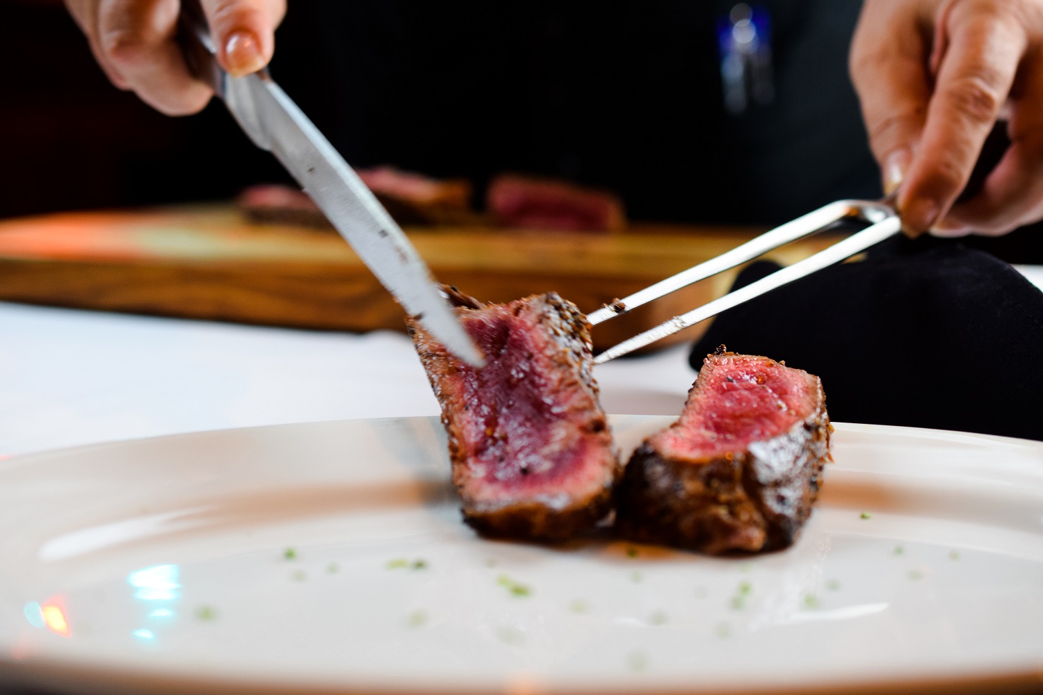 a server slicing a rare steak on a white plate