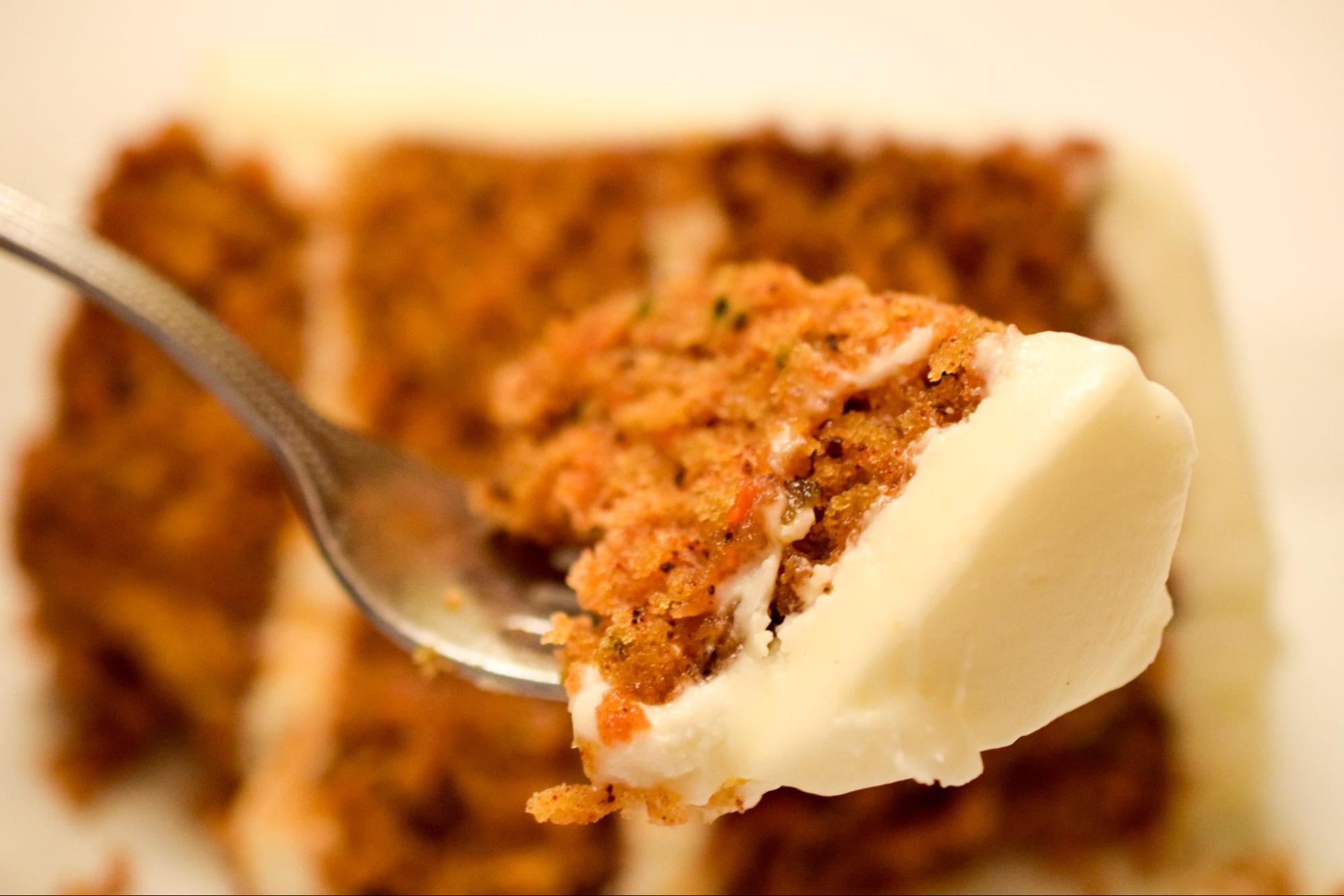 a forkful of carrot cake in front of a slice of carrot cake on a plate