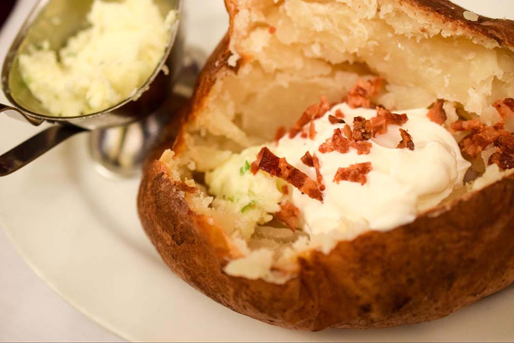 A baked potato with sour cream, chives, butter, and bacon bits on top.