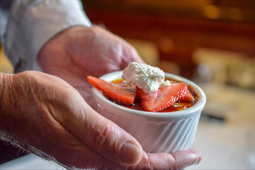 Christner's chef holding créme brulee topped with strawberries and whipped cream.