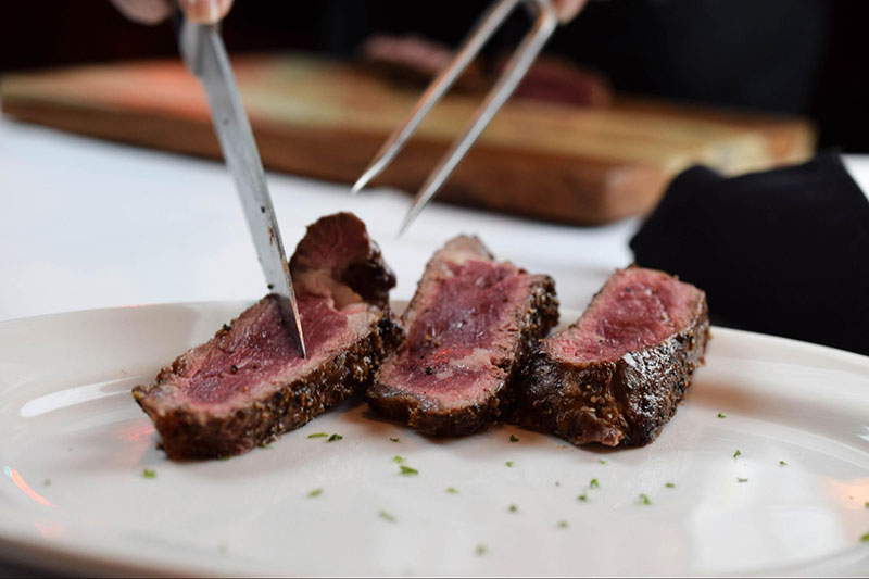 Steak being cut and placed on a plate. 