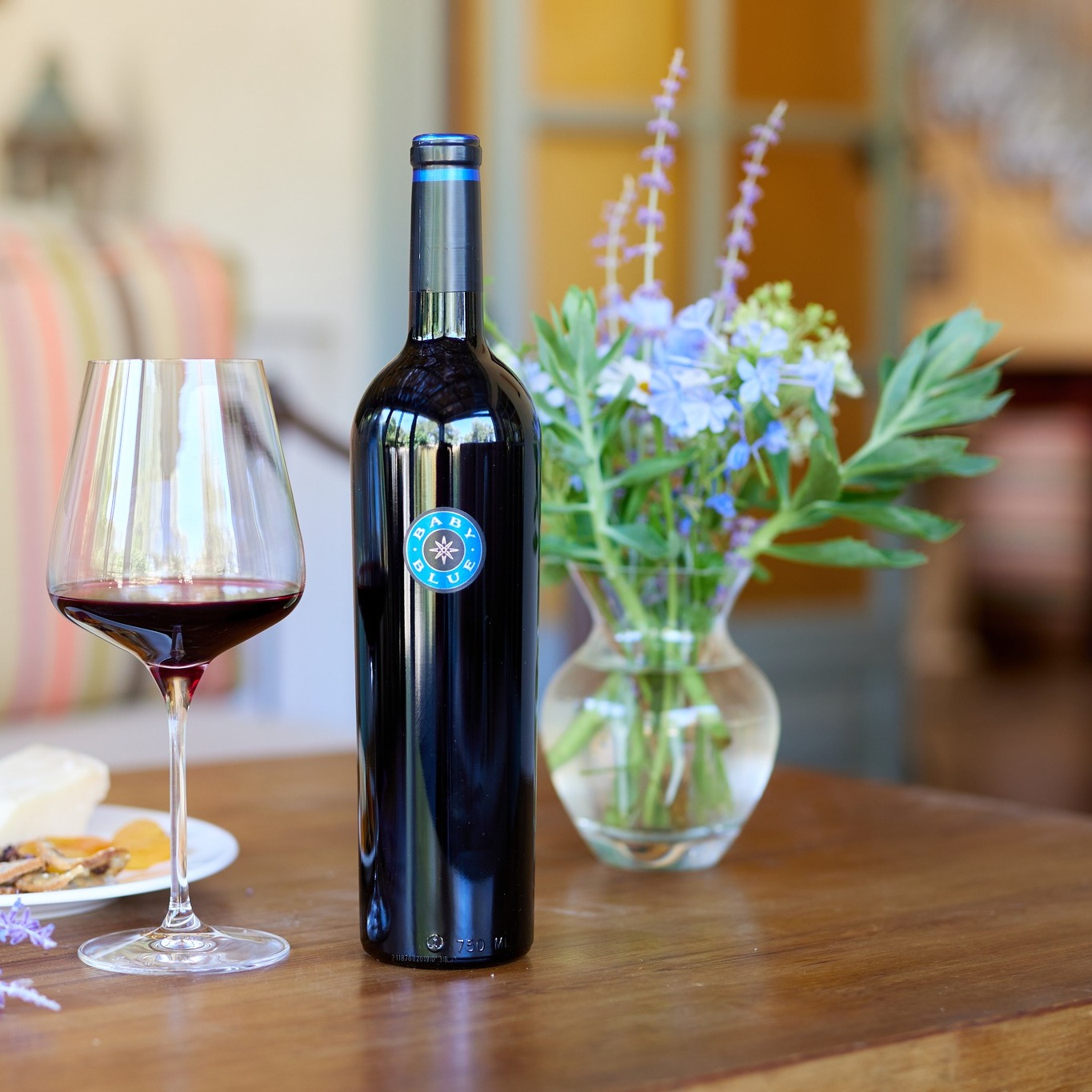 a bottle of Blue Rock Winery wine on a table next to a wineglass and a vase of flowers